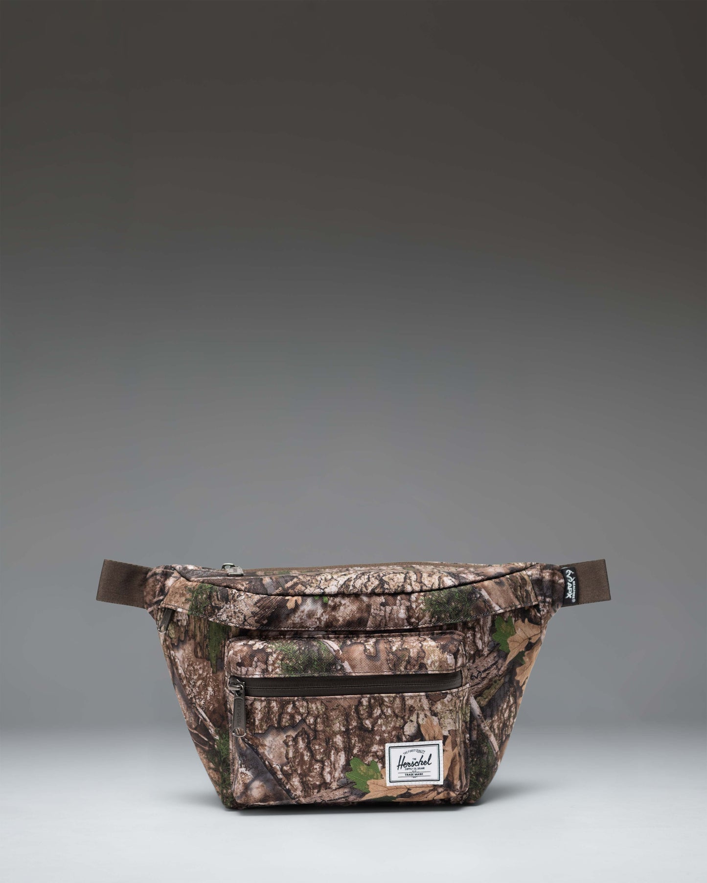 Herschel Supply Co. Pop Quiz Hip Pack in Realtree APX Camo pattern, showing the adjustable strap and front zipper pocket.