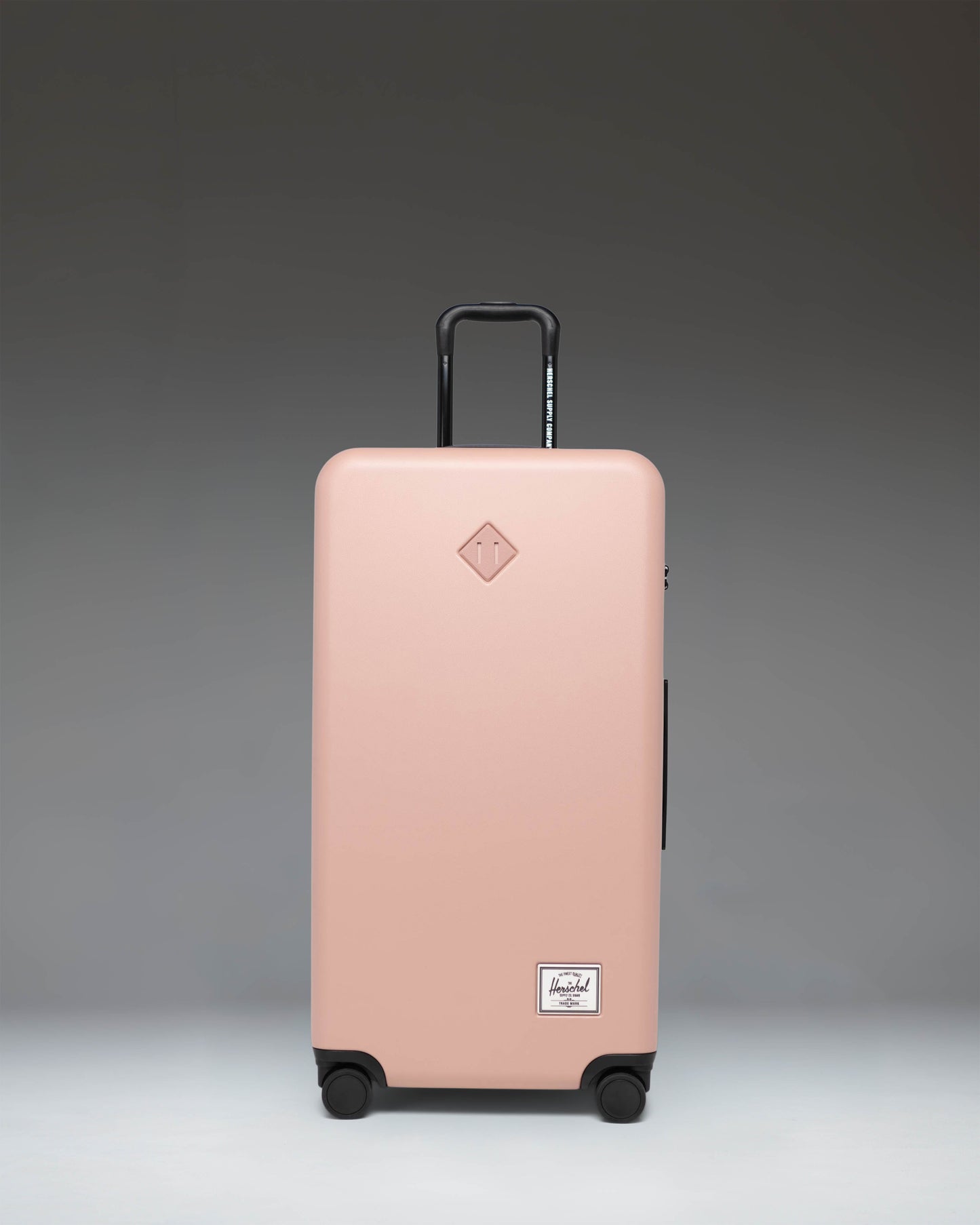 Herschel Heritage Hardshell Large Luggage in Ash Rose pink, featuring a durable textured exterior, trolley handle, and four wheels.