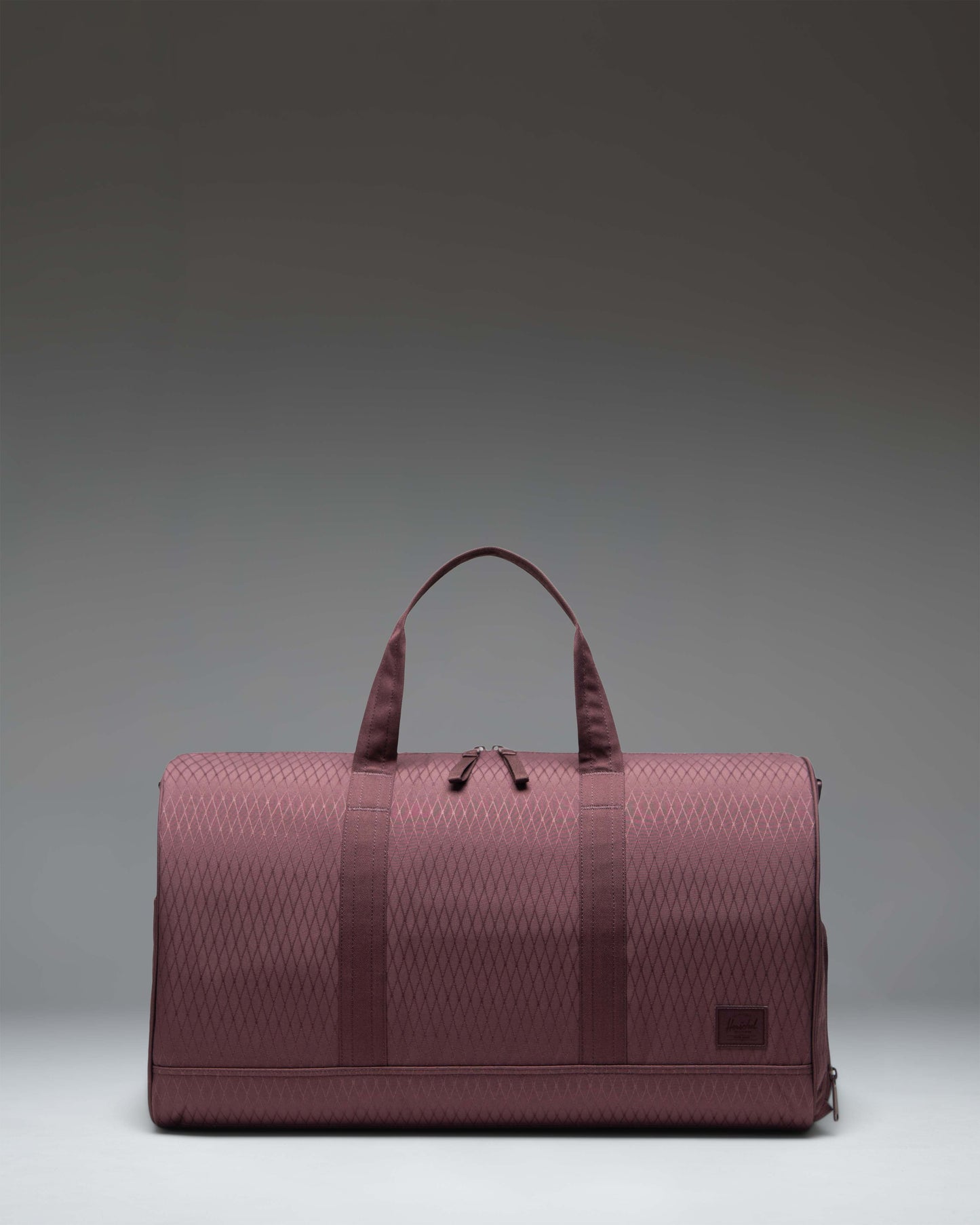 Herschel Novel Duffle bag in Huckleberry Diamond, a deep purple textured fabric with top handles, removable shoulder strap, and signature shoe compartment.