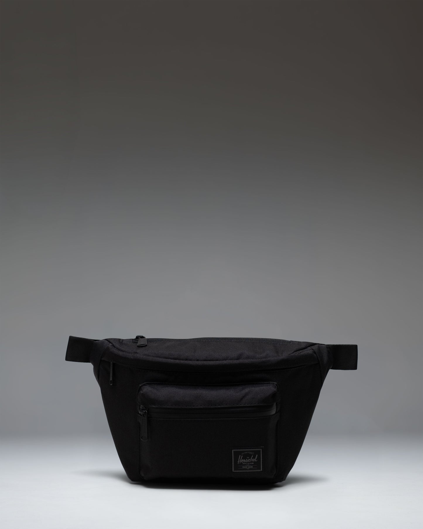Herschel Supply Co Pop Quiz Hip Pack in Black Tonal, showing the front view of the sleek, compact waist bag with zipper detail.