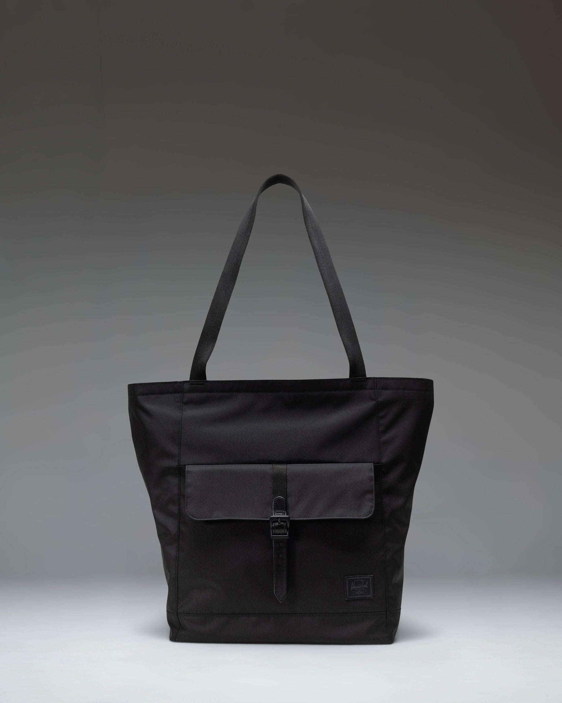 Herschel Retreat Tote bag in black, showcasing its clean design, dual carrying handles, and classic woven label on the front.