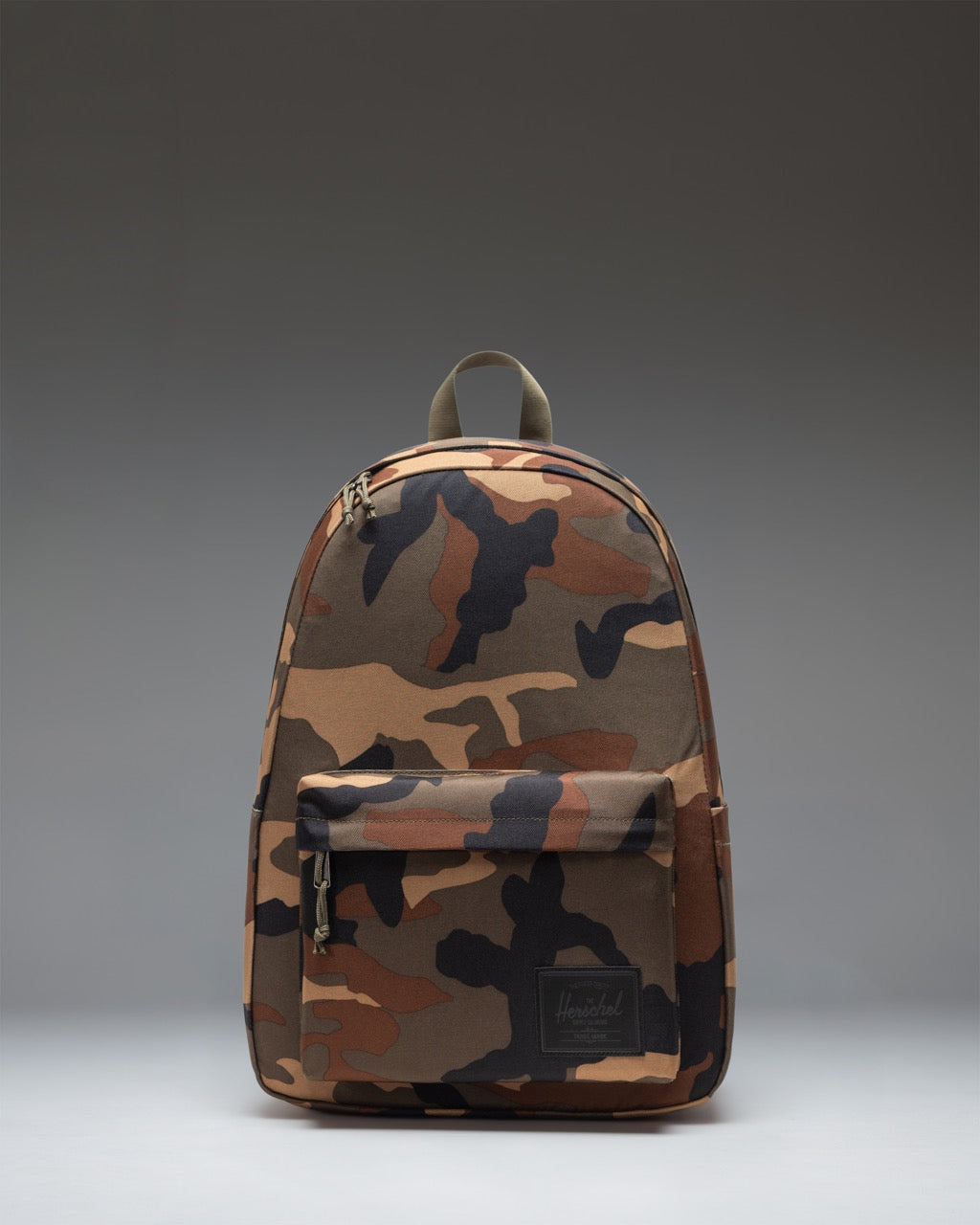 Herschel Classic XL Backpack in Woodland Camo/Black Label. Front view of the camouflage patterned backpack with a black zipper pocket.