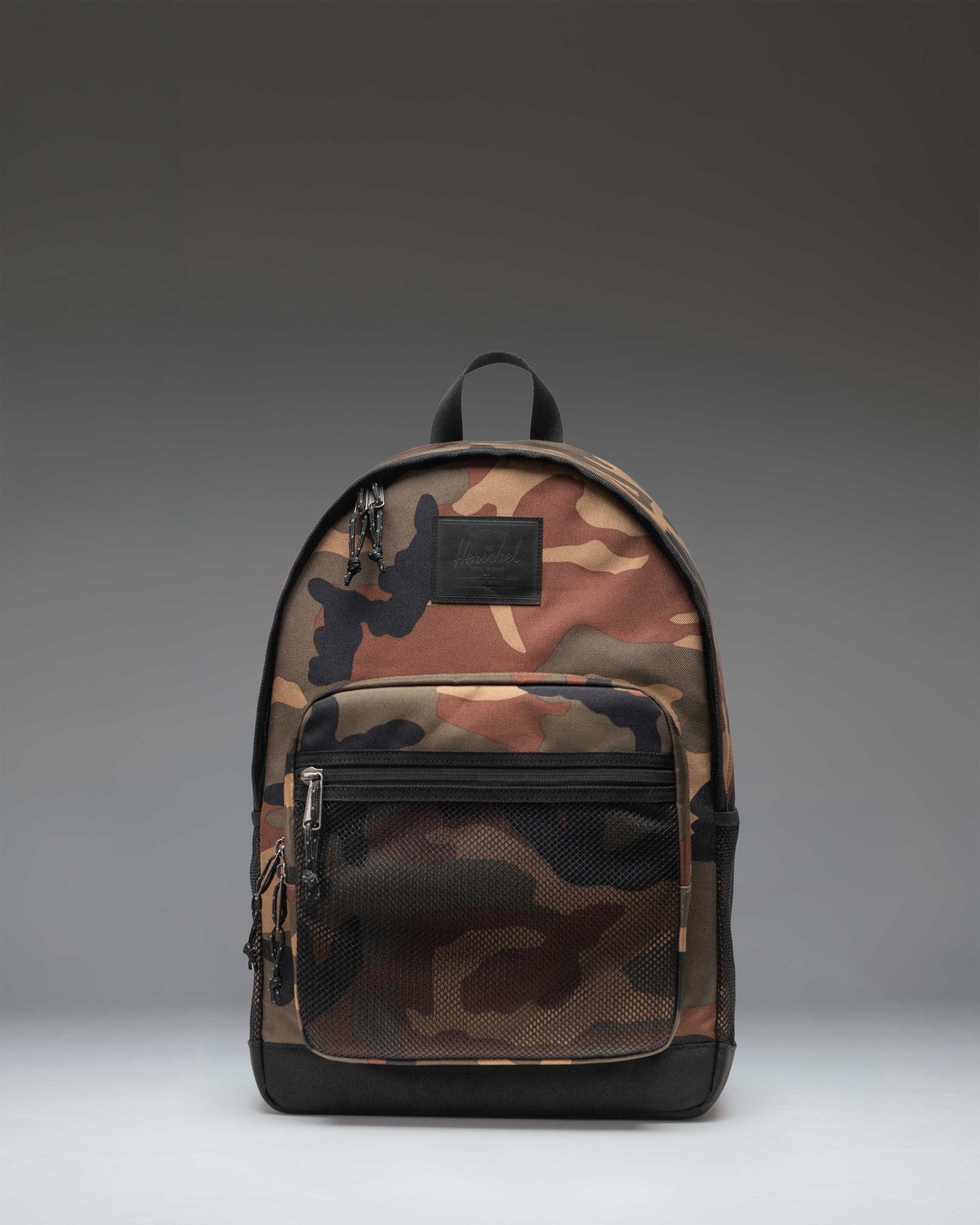 Herschel Supply Co. Kaine Backpack in Woodland Camo and black, showing the front view with straps, buckles, and mesh pockets.
