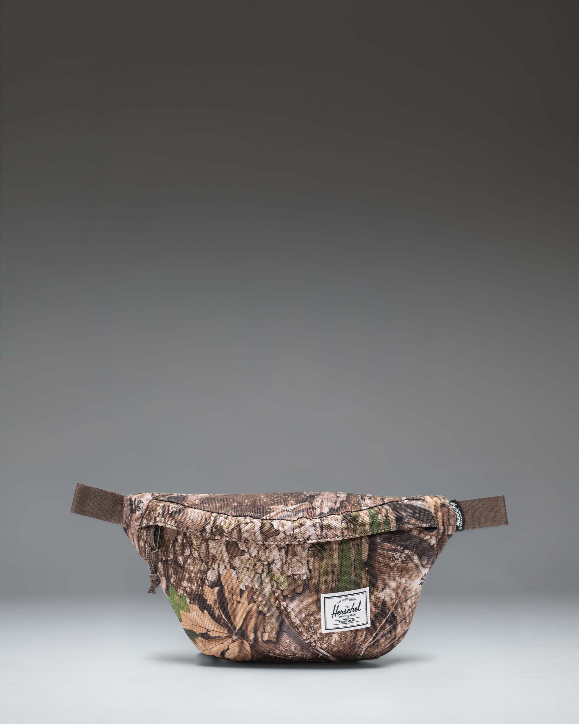 Realtree Herschel Classic Hip Pack in Realtree APX Camo, showing the front zippered pocket and adjustable strap.
