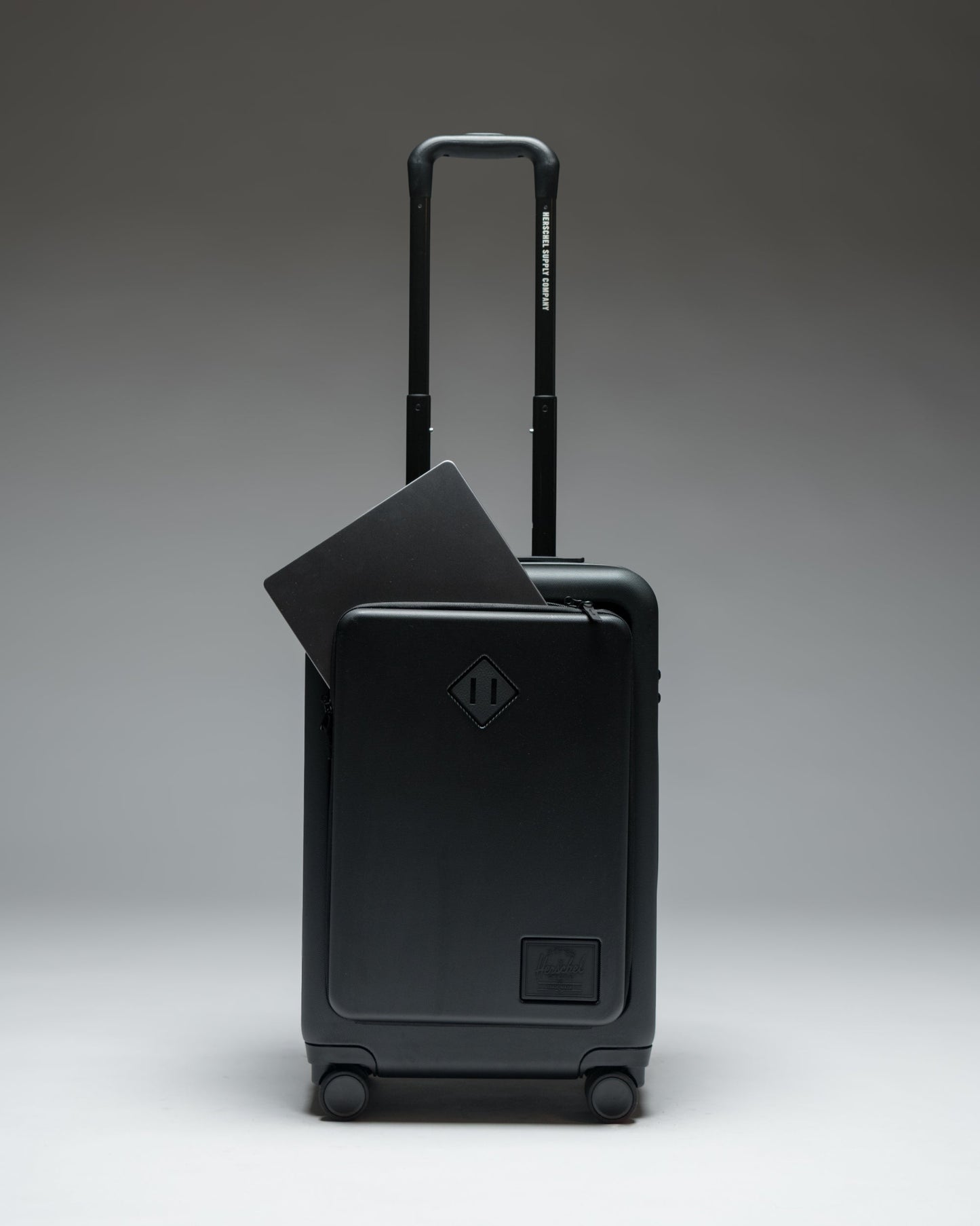 Herschel Heritage Hardshell Pro Large Carry On luggage in Black, shown from the front with a textured hard shell and retractable handle.