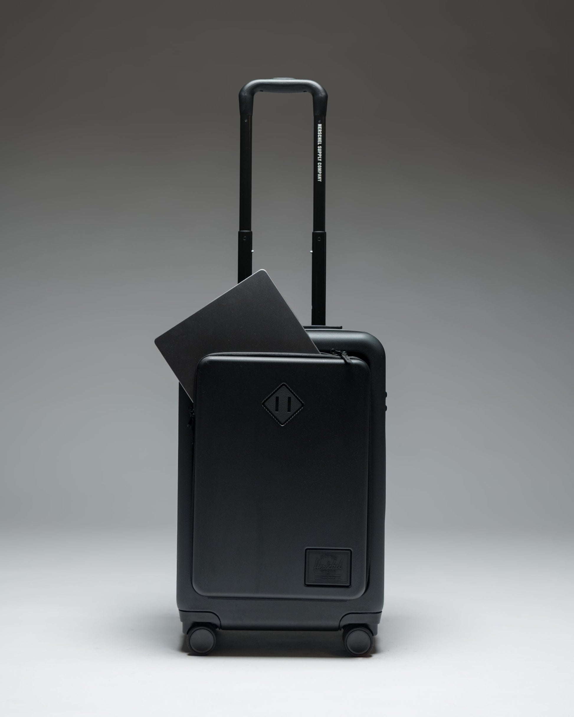 Herschel Heritage Hardshell Pro Large Carry On luggage in Black, shown from the front with a textured hard shell and retractable handle.
