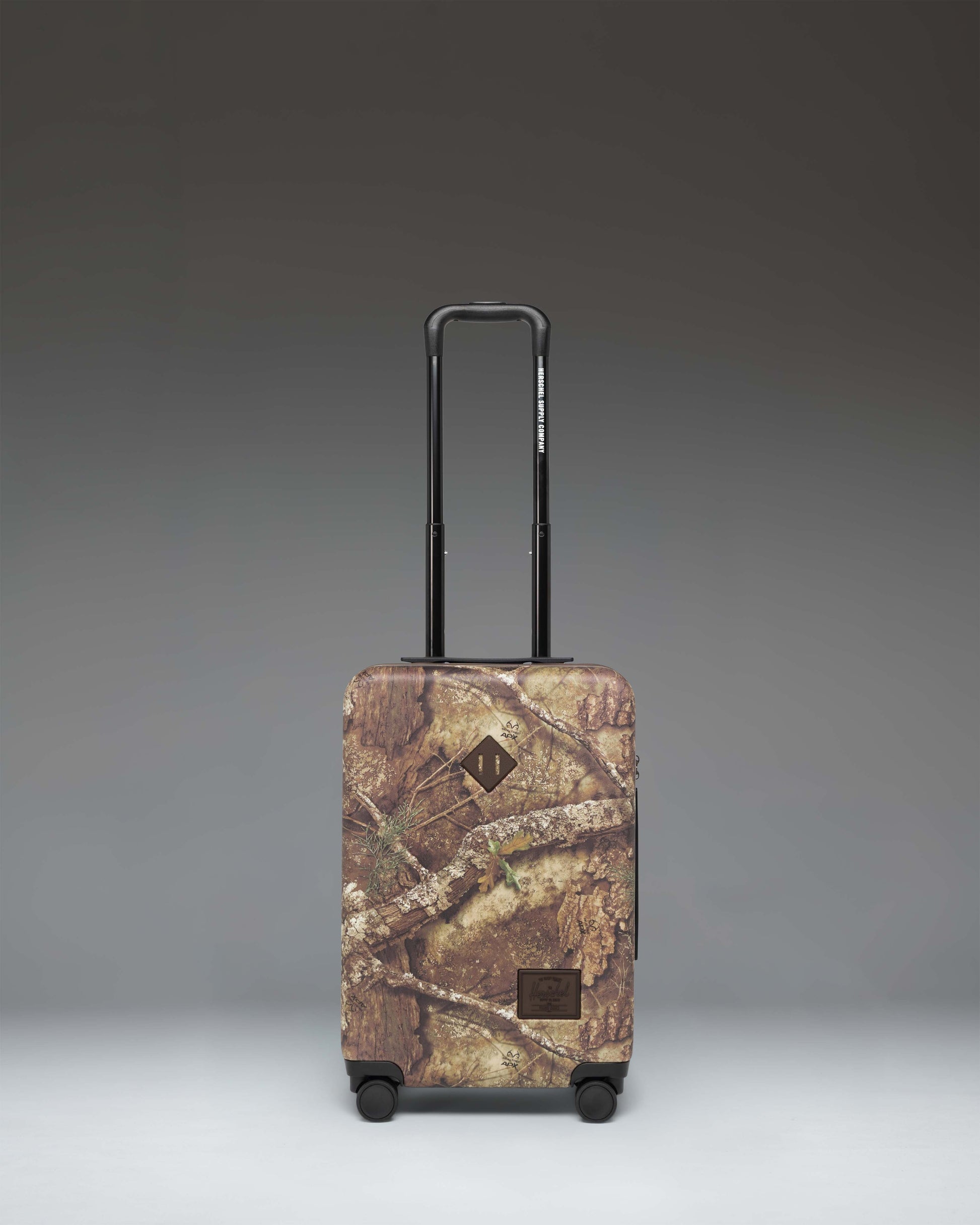 Herschel Heritage Large Carry-On Luggage in Realtree APX Camo pattern, showing the front view of the hard-shell suitcase.