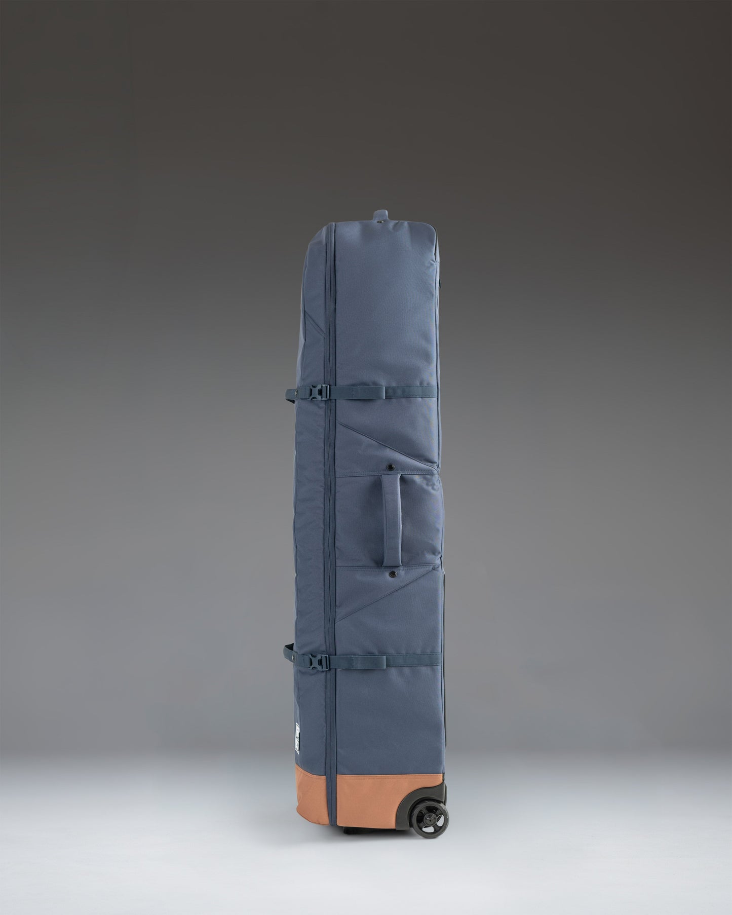 Herschel Heritage Golf Travel Wheelie Bag in Navy and Saddle Brown, showing a side view with wheels and a sturdy handle.
