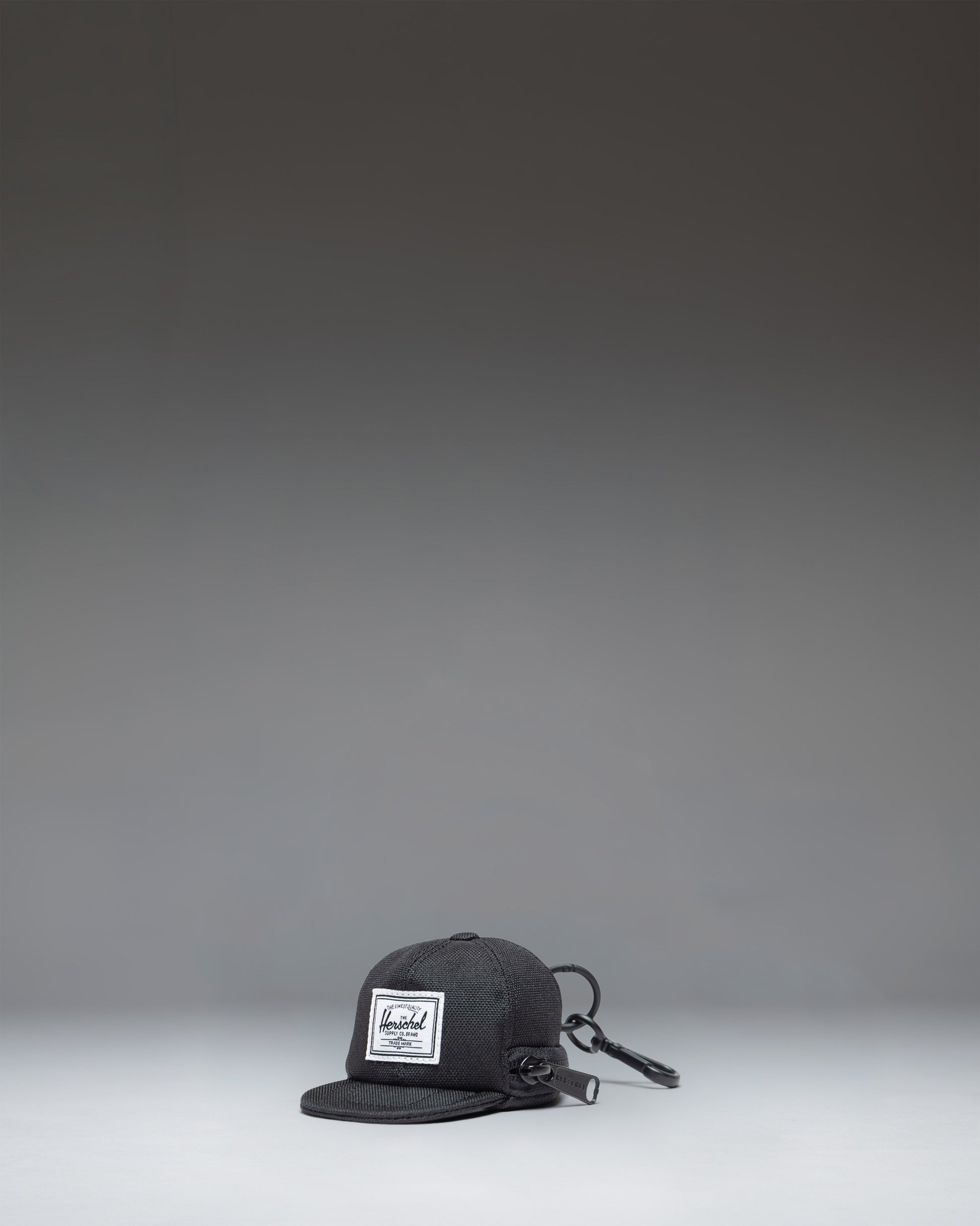 Herschel Supply Co. Sylas Classic Cap Bag Charm in black, showing the front view of a miniature baseball cap keychain accessory.